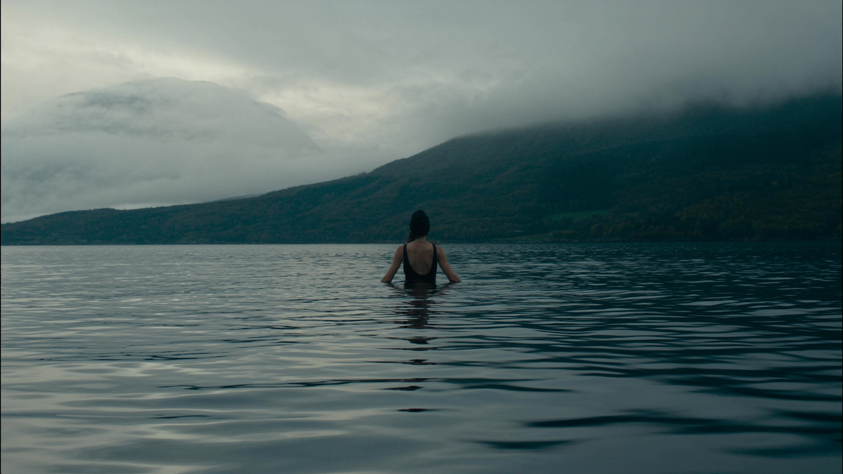 Bader i svart badedrakt står til livet i fjorden, sett bakfra