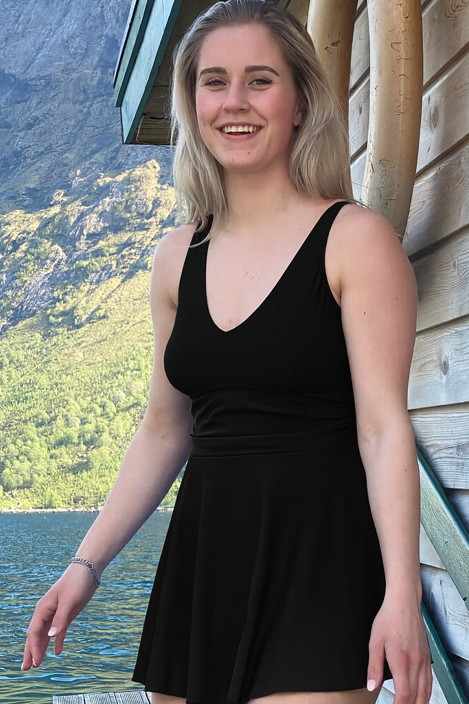 Dame som har på svart marilyn badekjole fra Fjord Vibes of Norway og såt på en brygge ved en flytende sauna i en norsk fjord