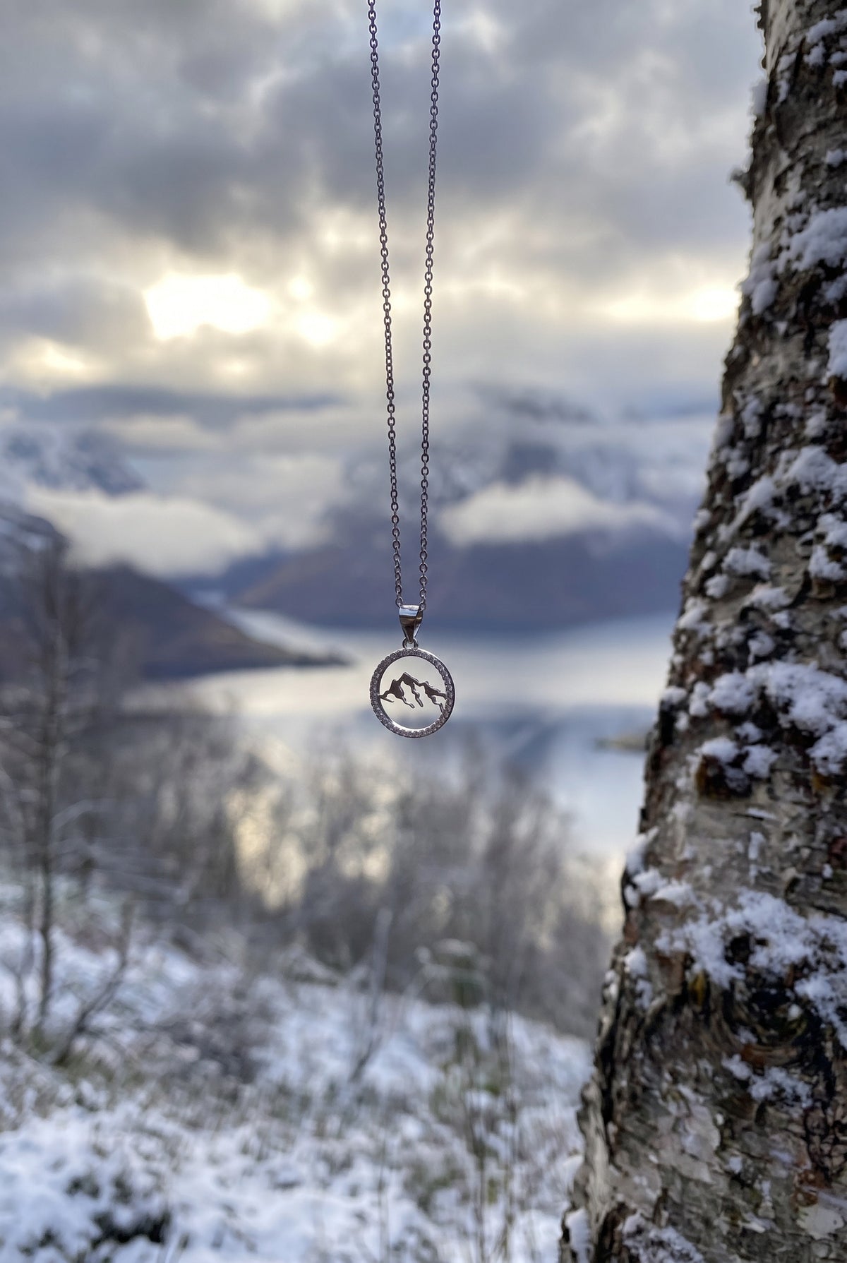 Tind fjellsmykke med zirkonsteiner fra Fjord Vibes hengende foran fjord og snødekte fjell på Sunnmøre