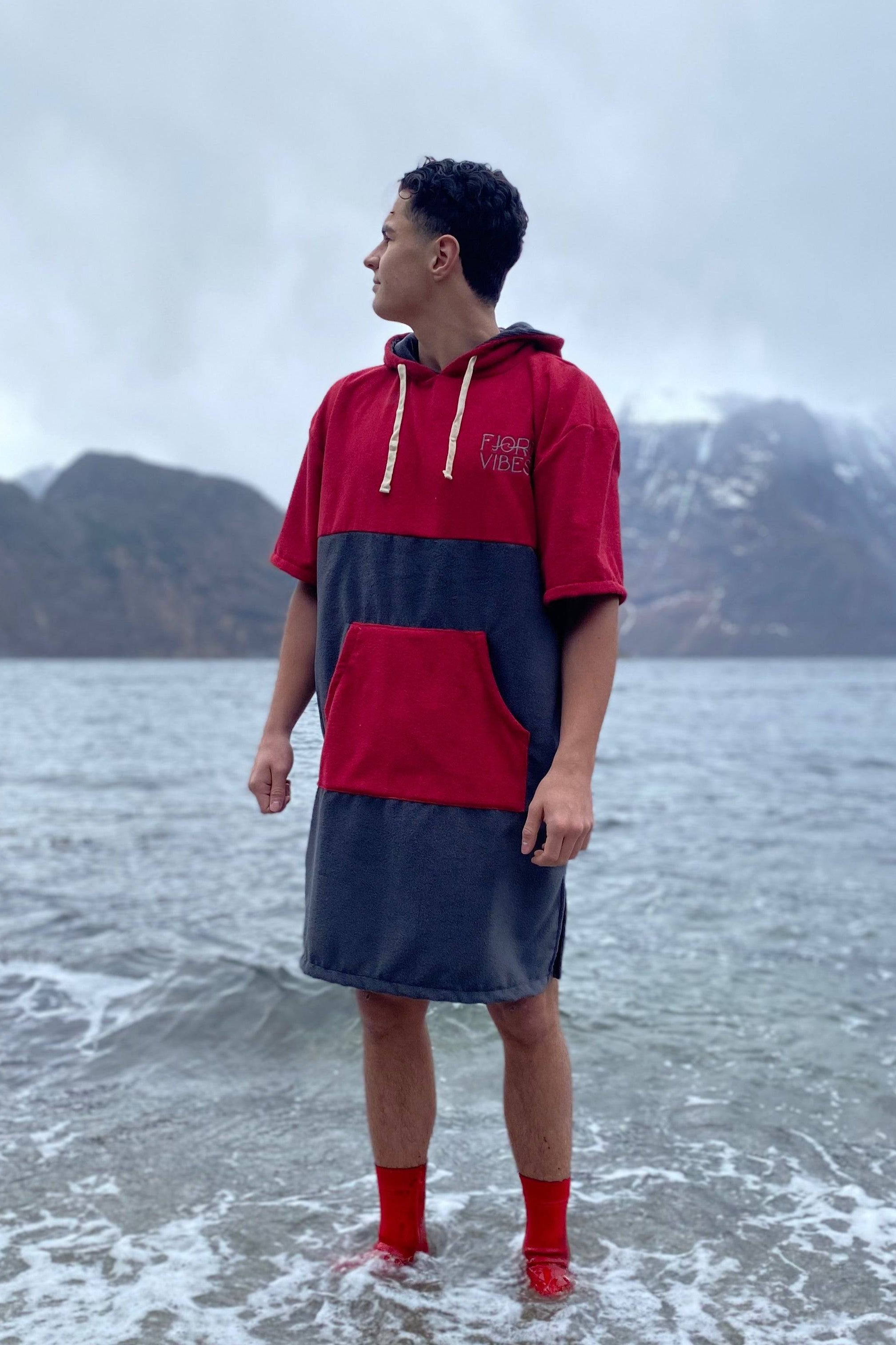 en mann som står i fjøra og ser mot fjellene. Han har på en rød og grå badeponcho for isbading