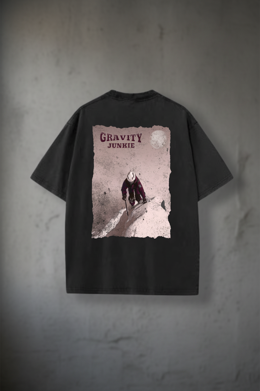 En t-skjorte i washed utførelse med bilde av en person som er på vei opp et fjell med stegjern og is-øks med teksten Graviy Junkie skrevet på ryggen. Mørk grå t-skjorte